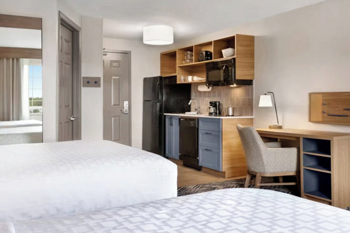 Une chambre d’hôtel comprenant un lit, un bureau avec une chaise, une kitchenette et une porte.