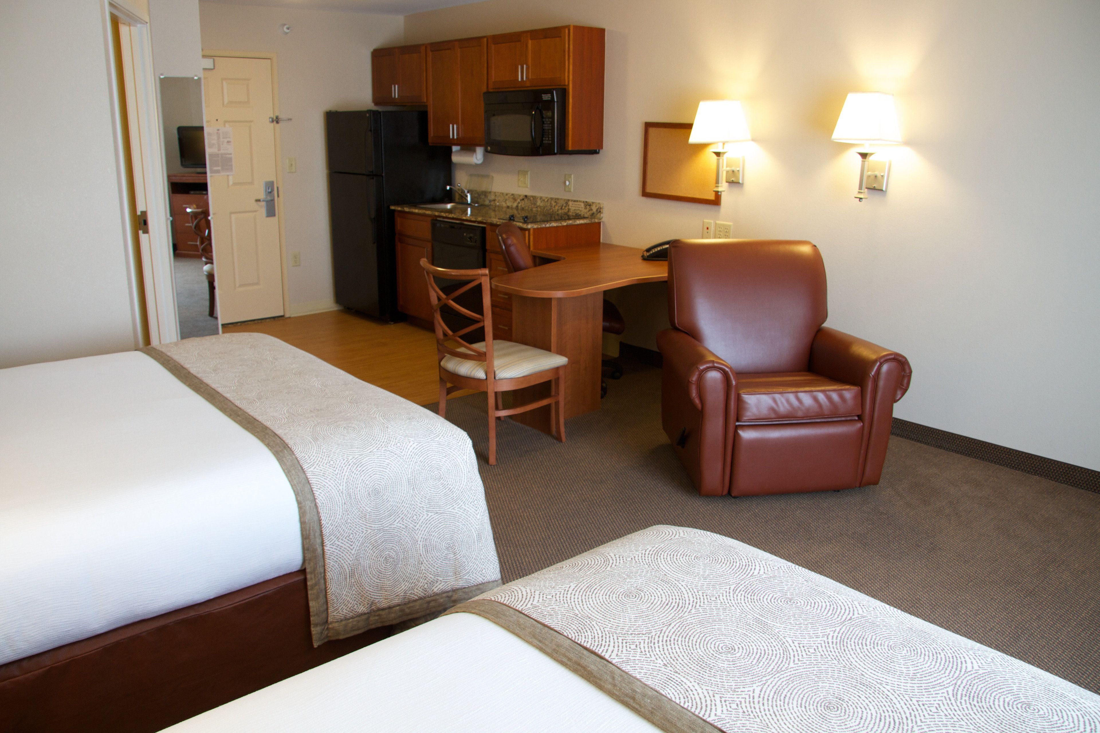A hotel room with two beds, a kitchenette, a dining area with a chair, and a leather armchair.