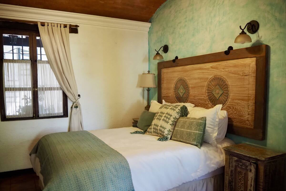 A neatly made bed with patterned pillows, a wooden headboard, and a nightstand with a lamp.