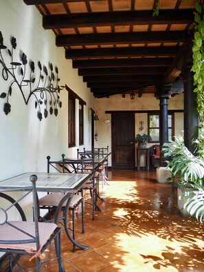 A covered patio area with tiled flooring, wooden tables and chairs, and decorative wall art. - Casa Madeleine Boutique Hotel & Spa (Antigua Guatemala)
