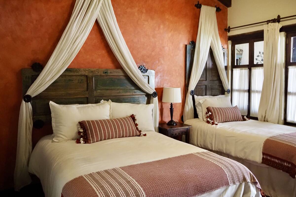 A room with two beds, each with a canopy, a wooden headboard, and a nightstand with a lamp.