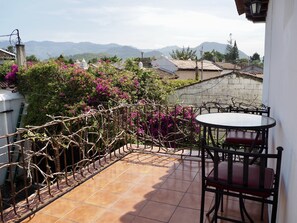 A terrace with a tiled floor, a round table with a red cushion, and a chair. There is a view of houses and mountains in the background. - Casa Madeleine Boutique Hotel & Spa (Antigua Guatemala)