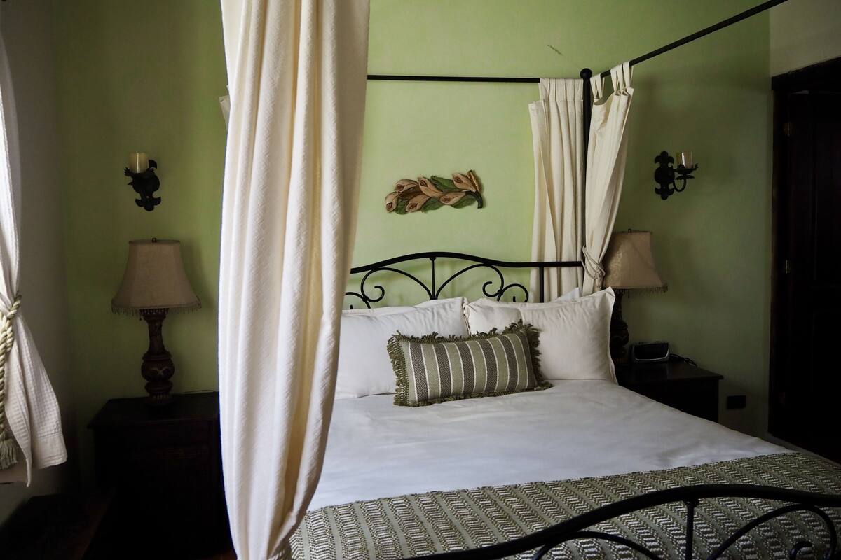 A bed with a canopy, a bedside table with a lamp, and a wall-mounted decoration.