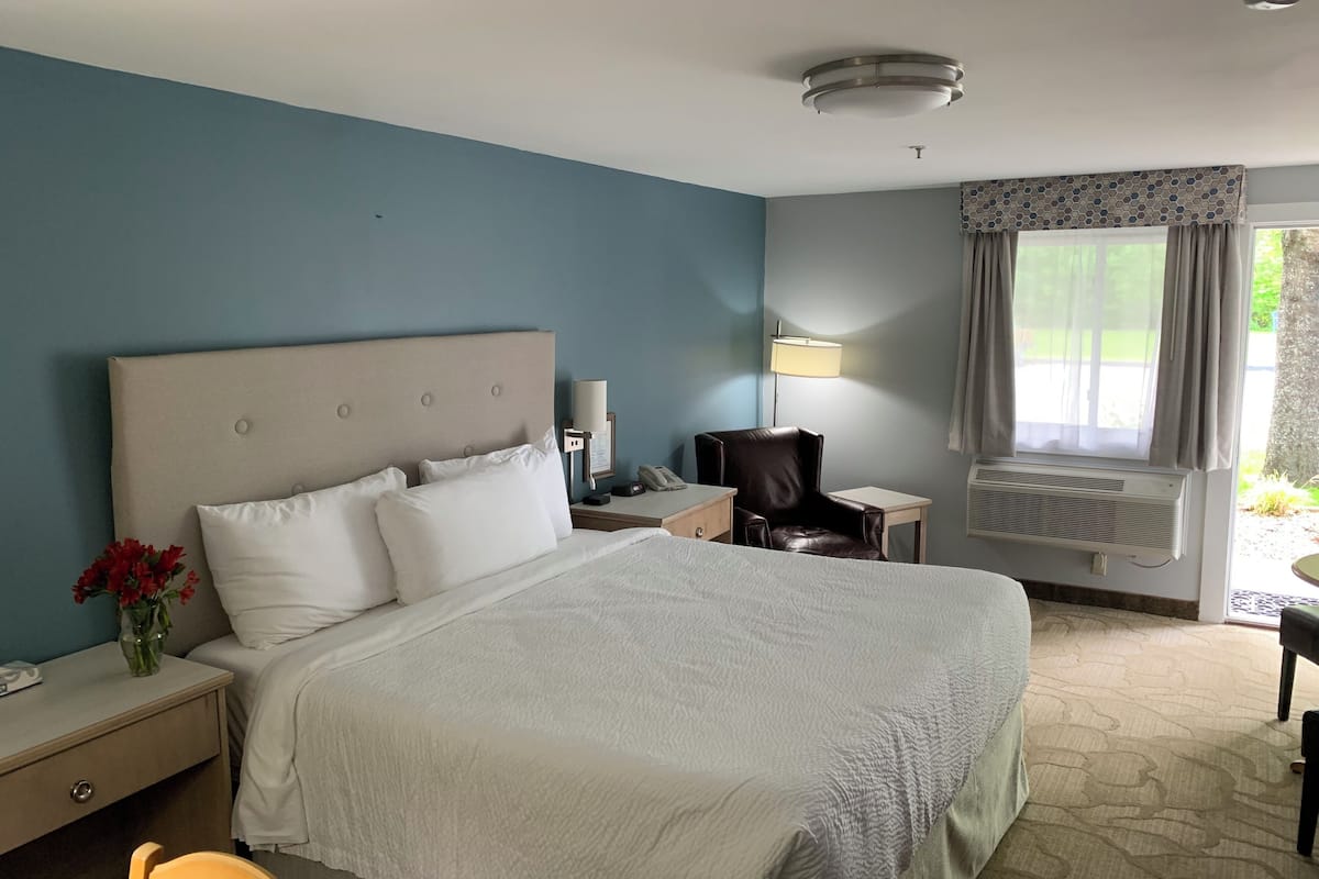 Une chambre d’hôtel avec un grand lit, une table de chevet, une chaise, un bureau, une lampe et une fenêtre avec des rideaux.