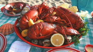 A large lobster on a plate with lemons and corn on the cob. - The Lodge at Turbat's Creek (Kennebunkport)