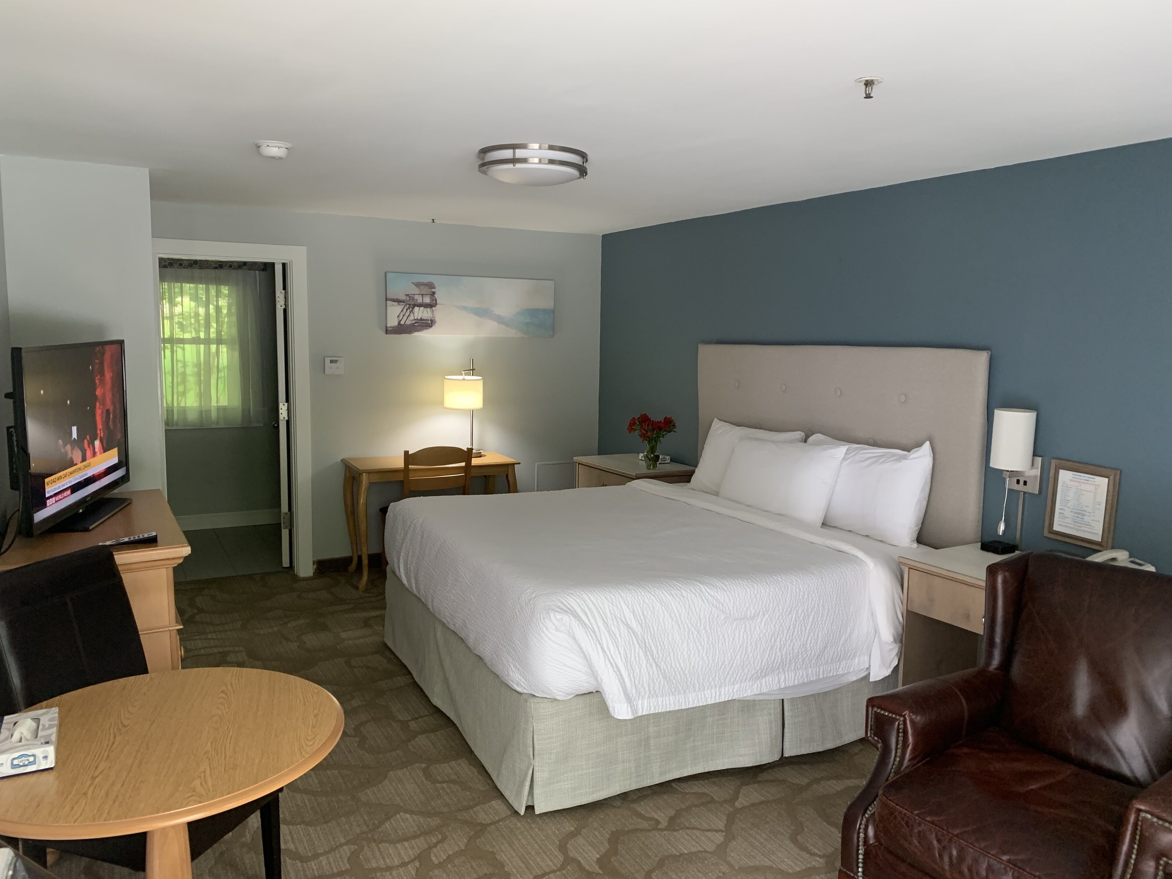 Habitación de hotel con una cama, un escritorio con lámpara, televisor, silla y mesa.