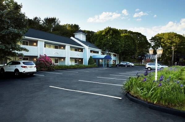 Un hotel con estacionamiento, entrada cubierta y fachada azul.
