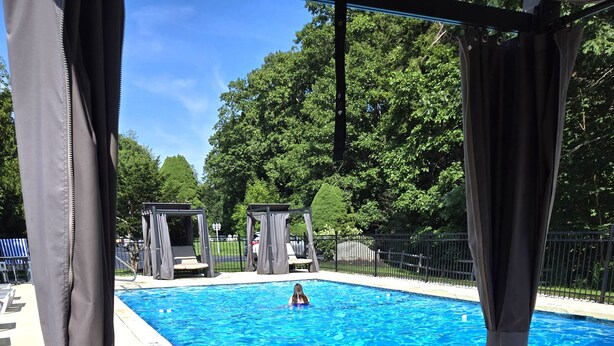 A clear blue pool with a person swimming, surrounded by lounge chairs and covered seating areas. - The Lodge at Turbat's Creek (Kennebunkport)