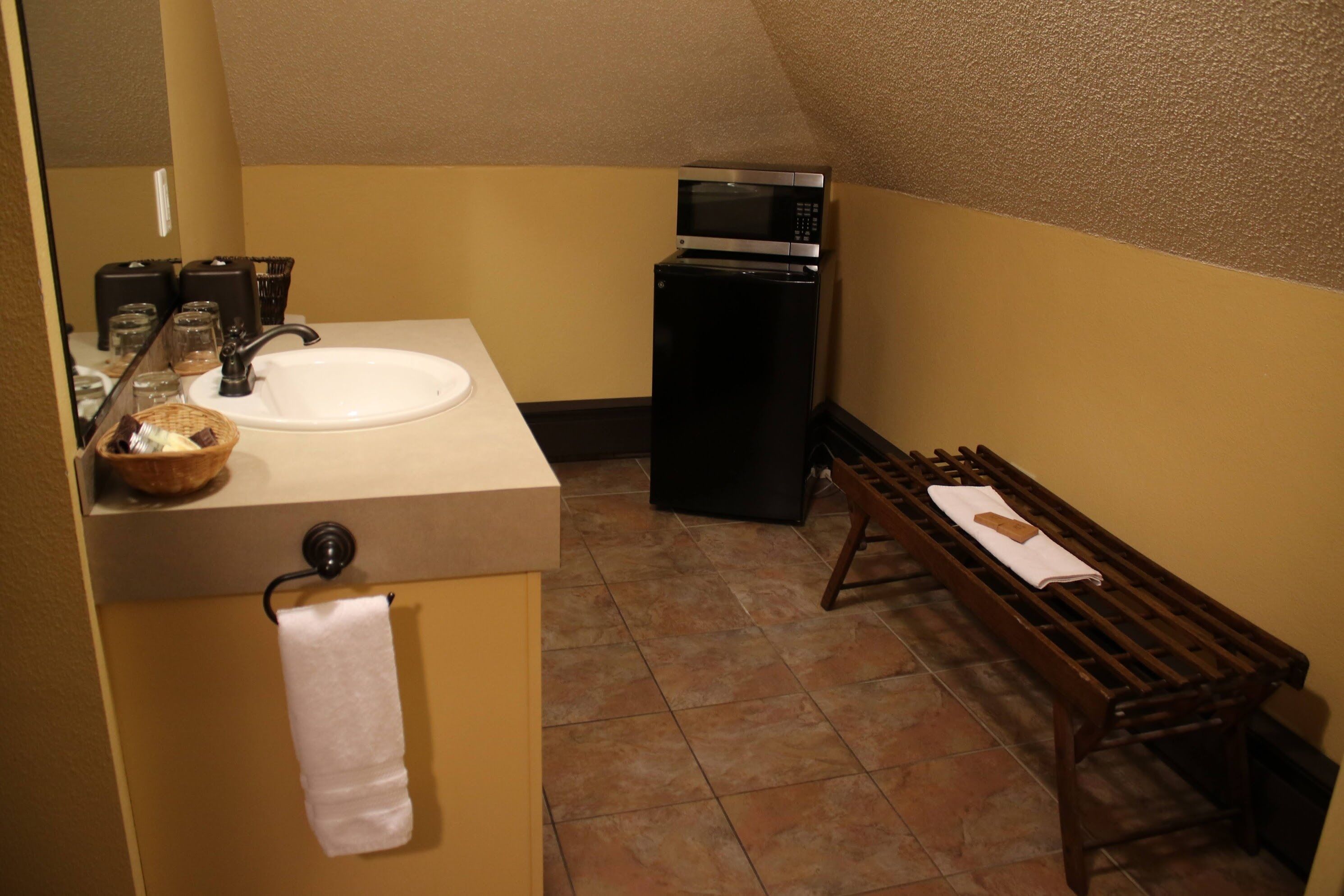 A compact bathroom with a sink, mirror, and a small refrigerator.