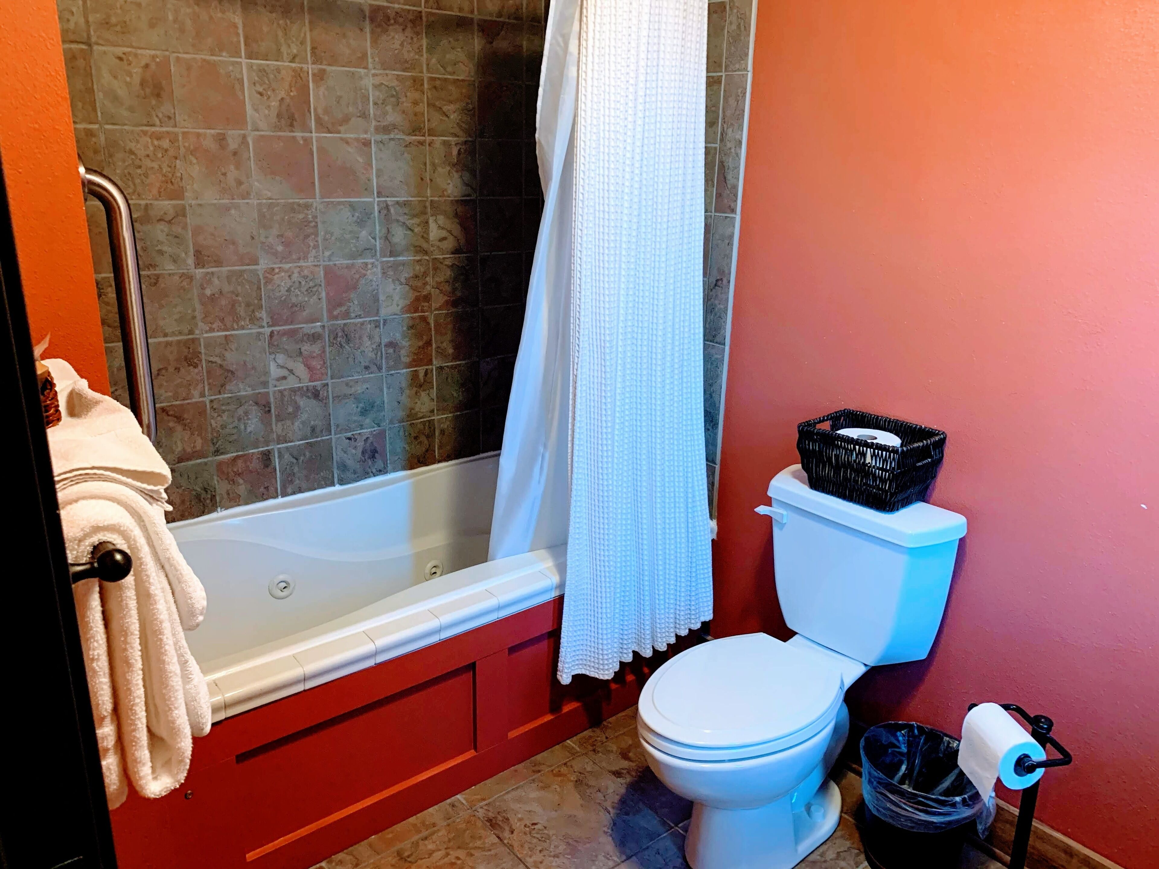 A bathroom with a bathtub, toilet, and a trash bin.