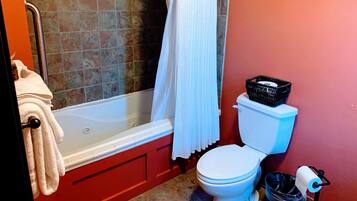 A bathroom with a bathtub, toilet, and a trash bin.