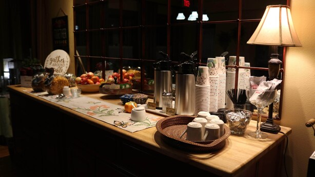 A breakfast bar with various food items, coffee and tea stations, and a decorative sign. - Iowa House (Ames)