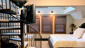 A bedroom with a bed, a staircase, a TV mounted on the wall, and a skylight. - Iowa House (Ames)