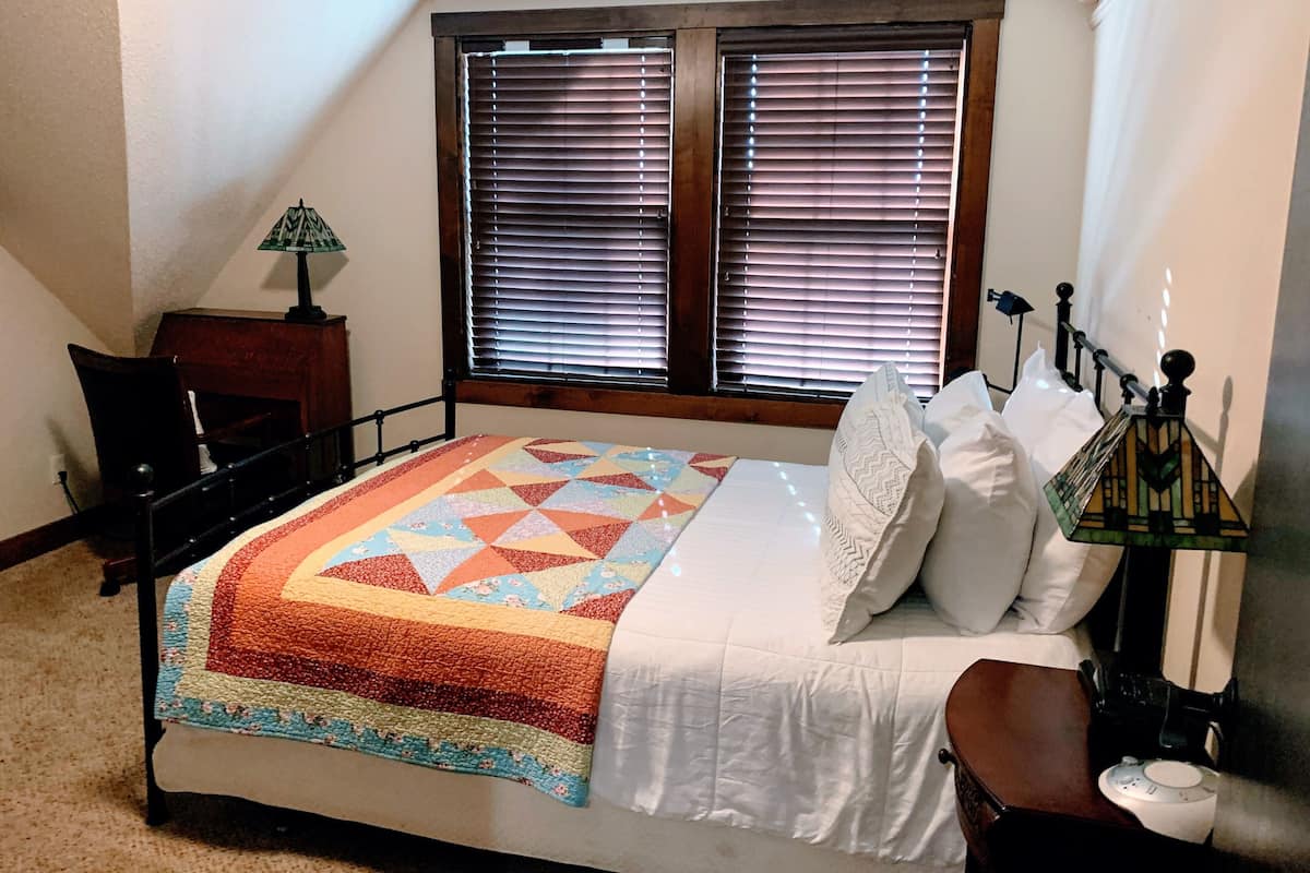 Un dormitorio con cama, escritorio y ventana con persianas.