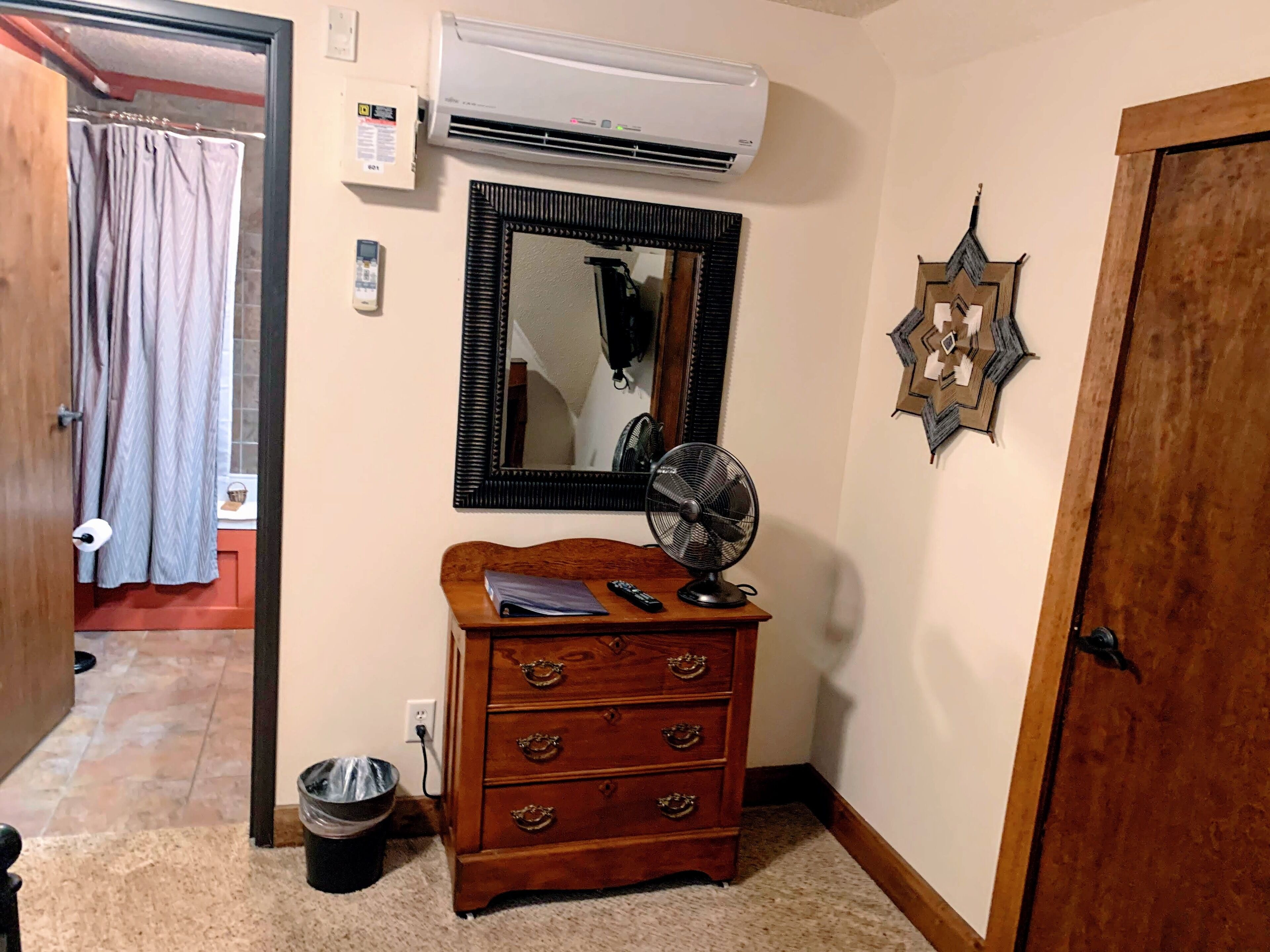 Una habitación con un aparador de madera, un espejo, un ventilador y un equipo de aire acondicionado en la pared.