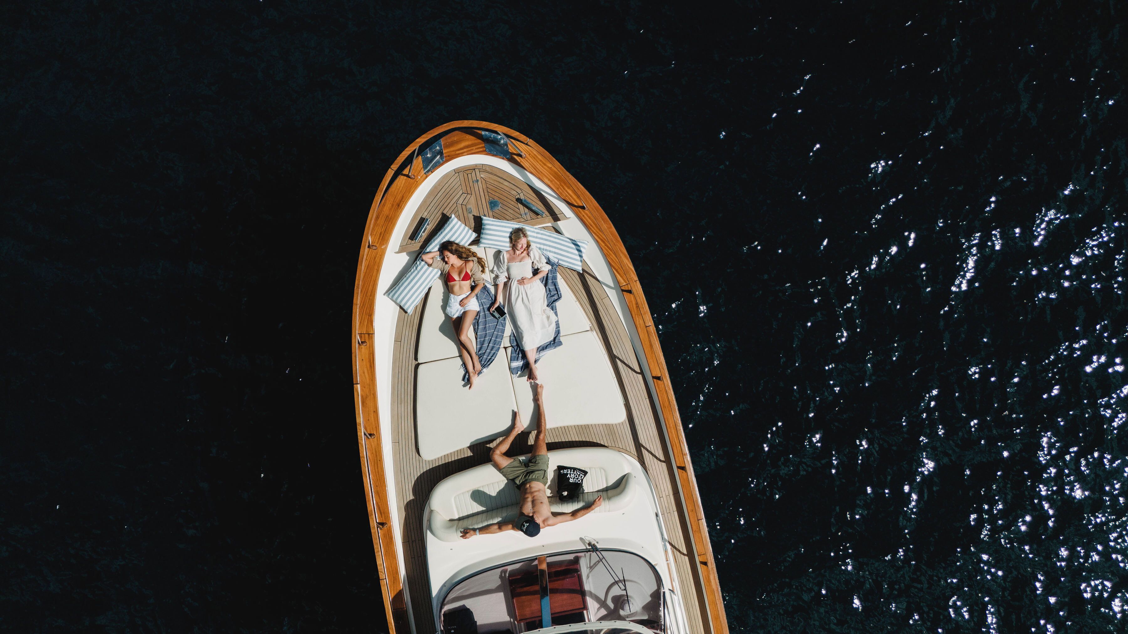 A boat with a wooden deck, a white interior, and a person lying on the deck.