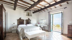 Un dormitorio con cama, banco, escritorio y vistas a través de un ventanal abierto.