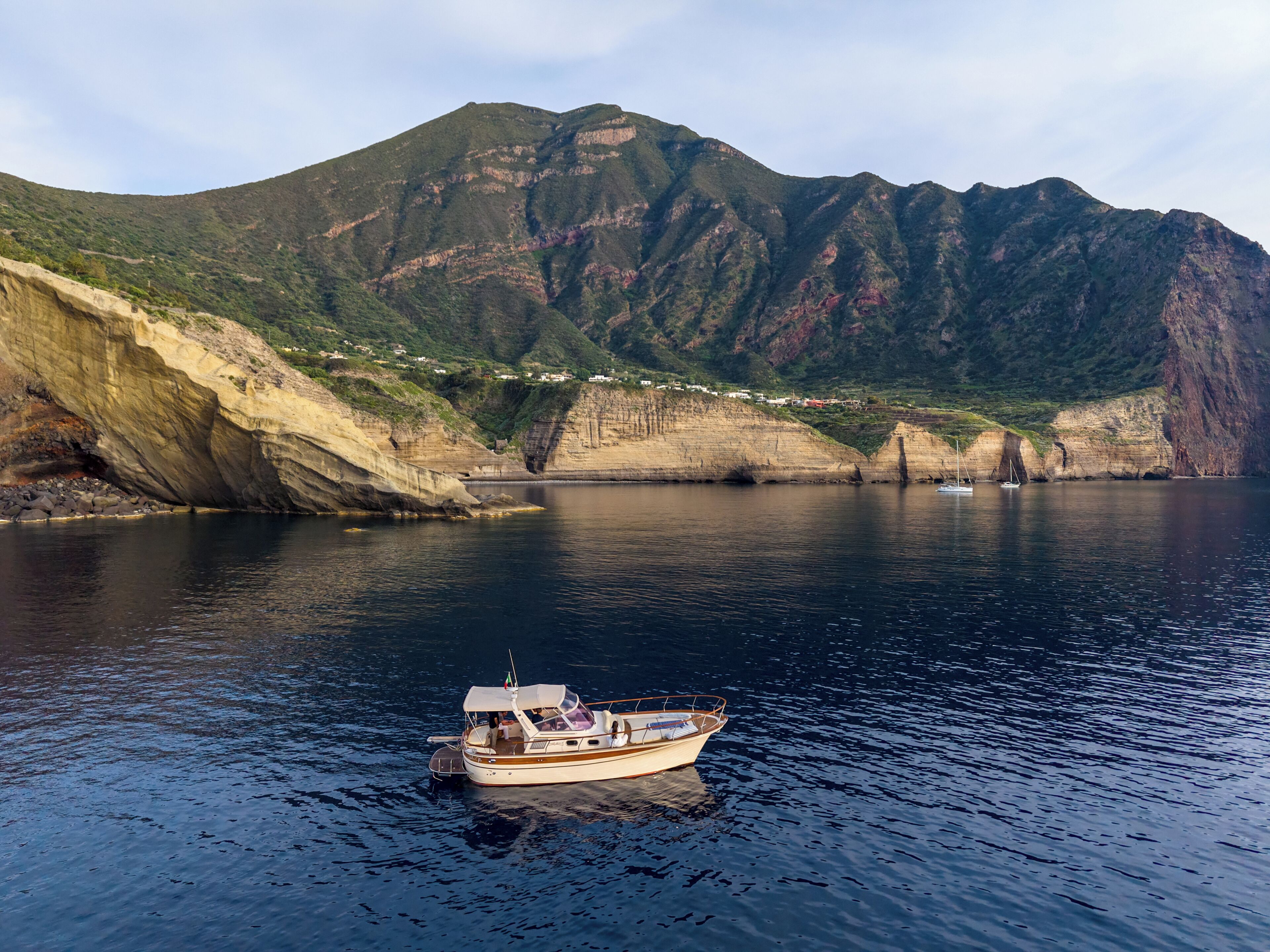A boat on calm water with a mountainous backdrop and a coastal village.