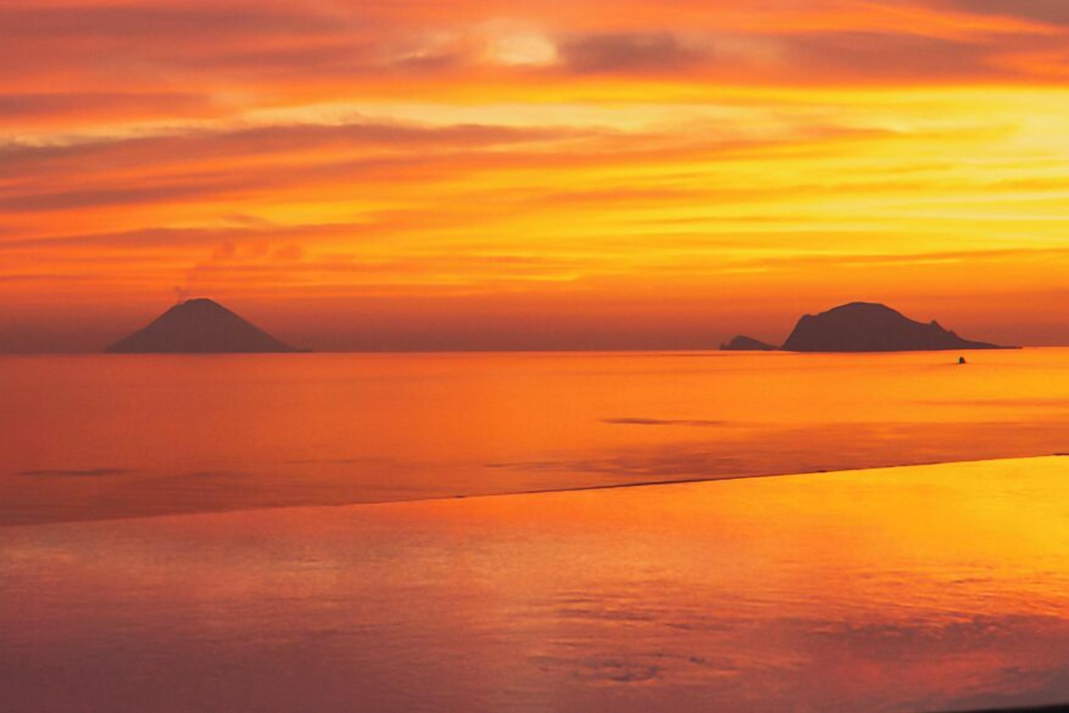 A sunset over a calm sea with two distant islands.