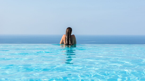 Una persona de pie en una piscina azul cristalina con vista al océano.