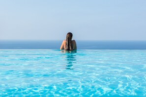 A person standing in a clear blue pool with a view of the ocean.
