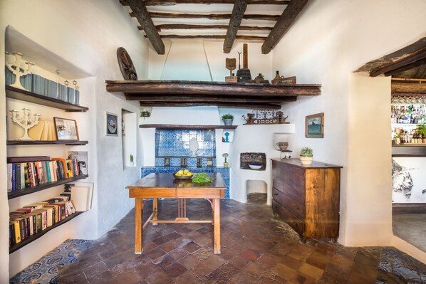 Una cocina rústica con vigas de madera a la vista, salpicadero de azulejos y estantes con libros y objetos decorativos.
