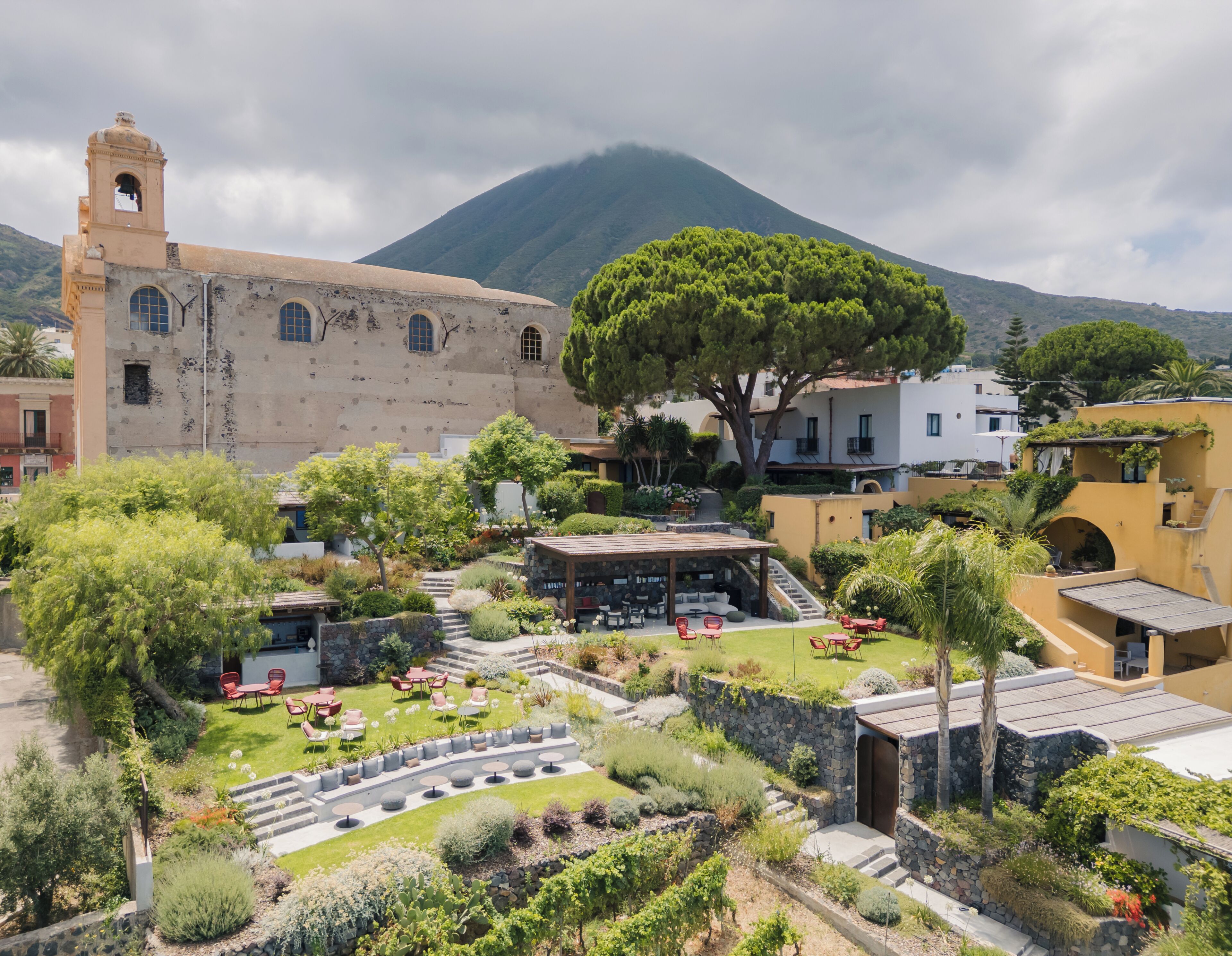 Un patio con mesas al aire libre, un árbol grande y un edificio histórico con un campanario.