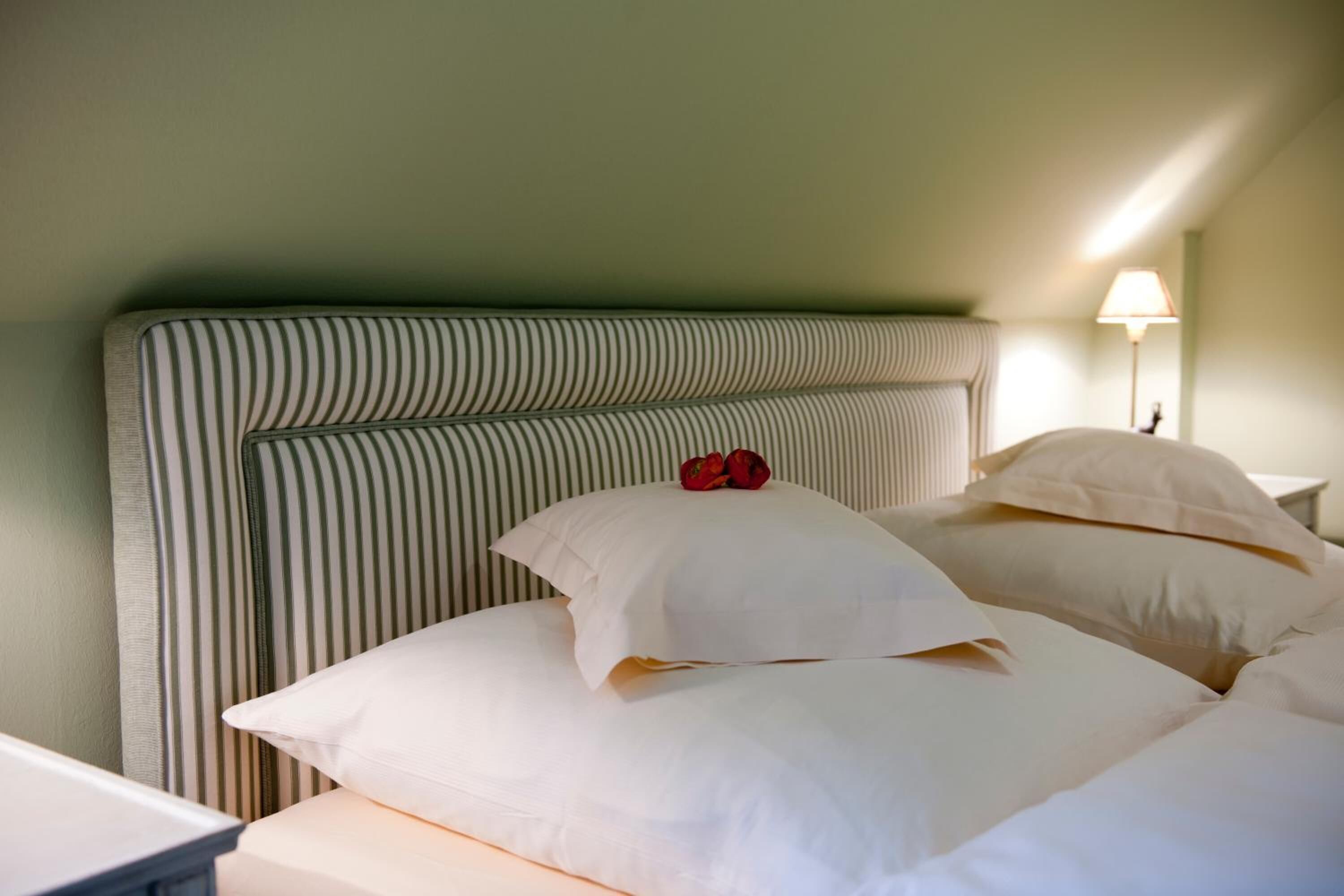 A bed with striped headboard and white pillows, a bedside lamp, and a green wall.