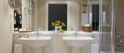 A bathroom with two sinks, a mirror, a shower, and a vase with flowers.