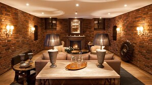 A cozy lounge area with a brick wall, a fireplace, a sofa, and two lamps.