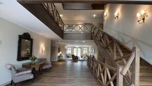 A spacious interior with a wooden staircase, a dining area with a round table and chairs, and a large mirror on the wall.