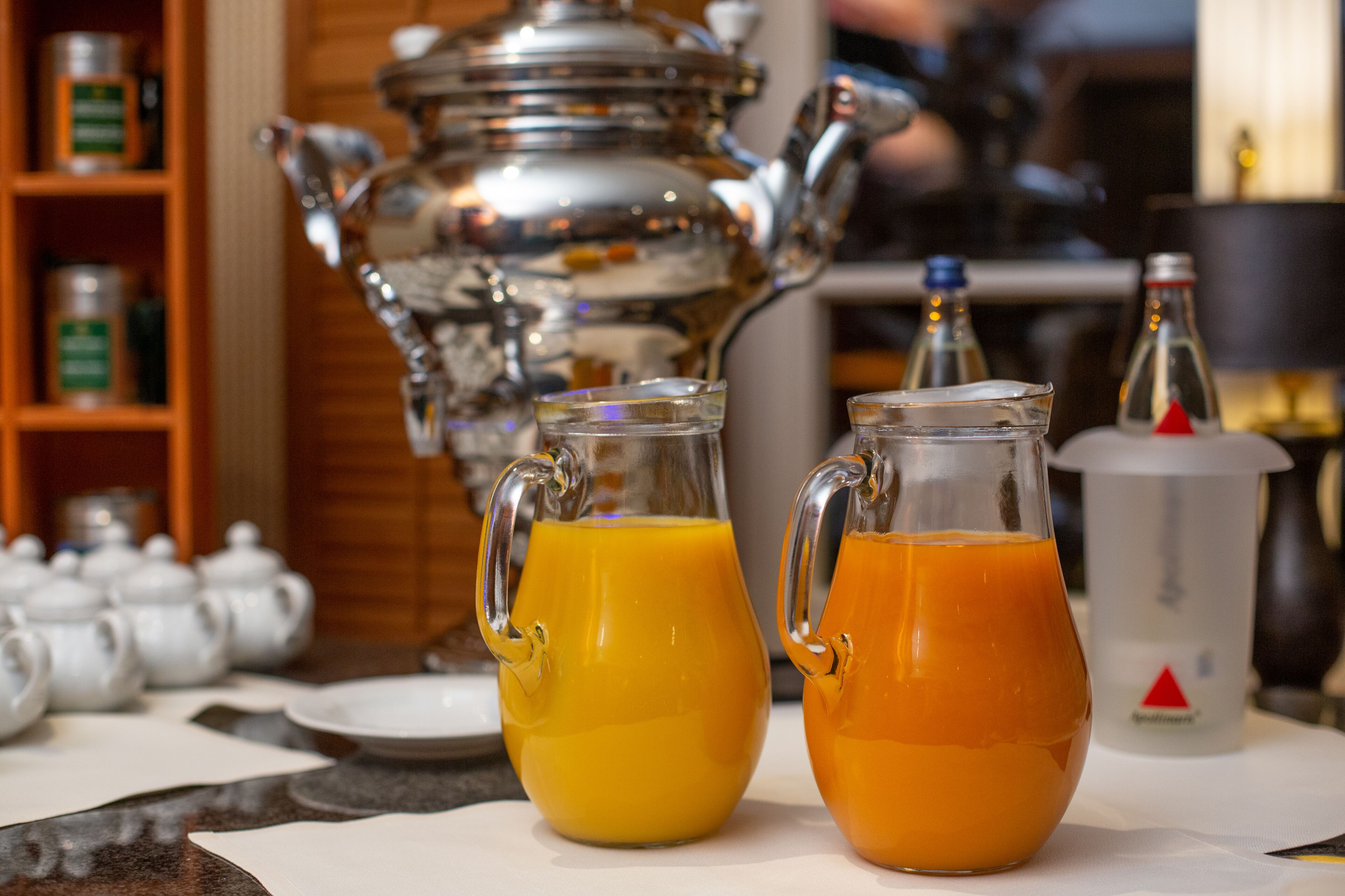 A breakfast setting with two pitchers of orange juice, a teapot, and a coffee pot on a table.