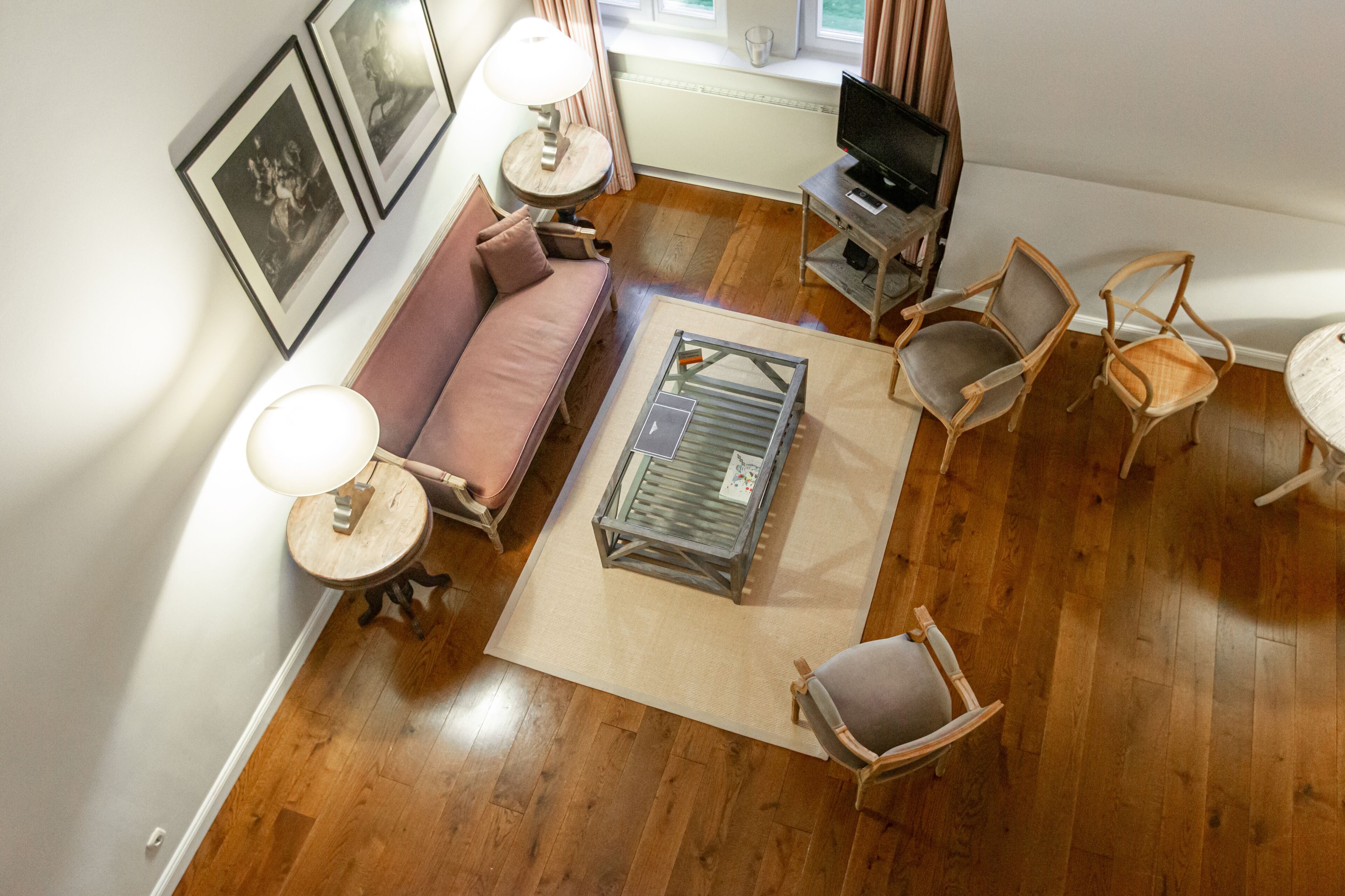 Uma sala de estar com sofá, poltronas, mesa de centro, televisão e quadros nas paredes.