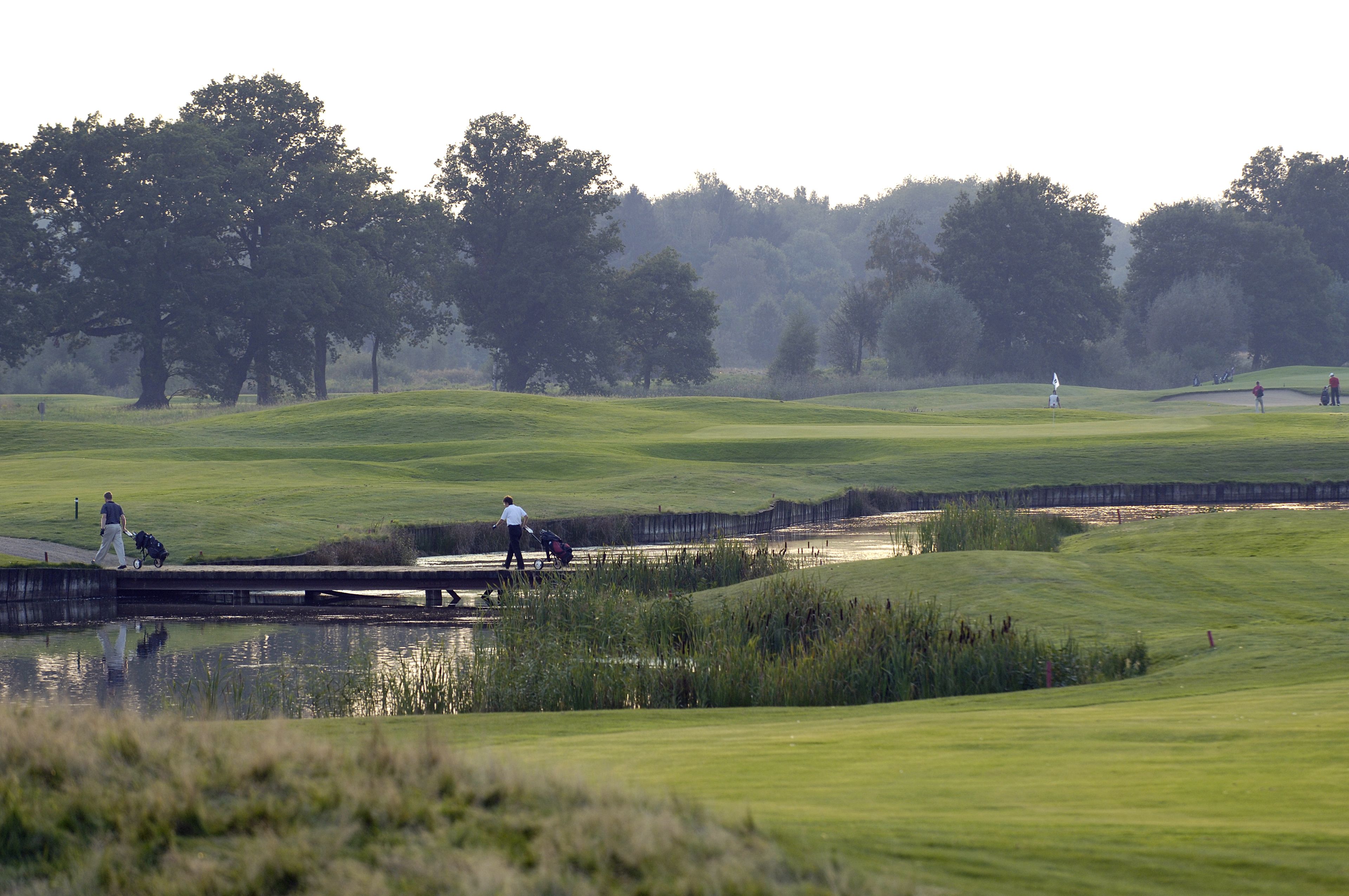 Een golfbaan met een waterpartij, bomen en een brug.