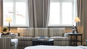 Ein Hotelzimmer mit einem Bett, zwei Sesseln, einem Sofa, einem kleinen runden Tisch und zwei Lampen.
