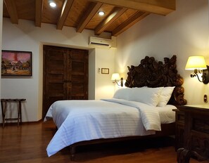 A bedroom with a wooden bed, a large wooden door, an air conditioning unit, a wall-mounted lamp, and a framed picture on the wall. - Hotel Mi Solar (Uruapan)