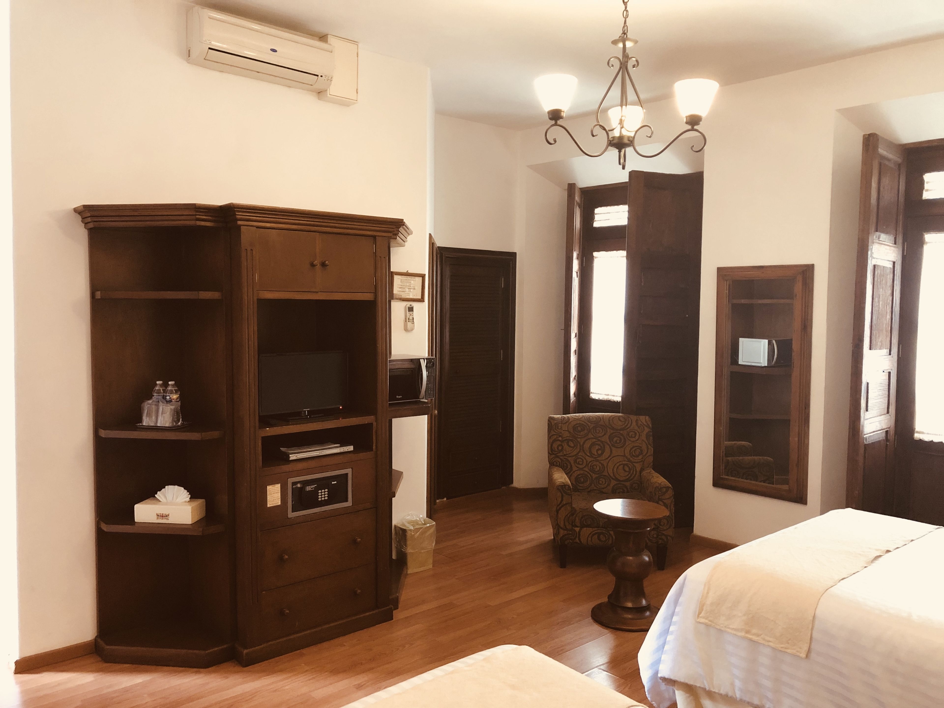 Una habitación de hotel con un armario de madera, una silla, una mesita redonda y una cama.