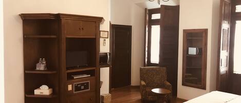 A hotel room with a wooden wardrobe, a chair, a small round table, and a bed.