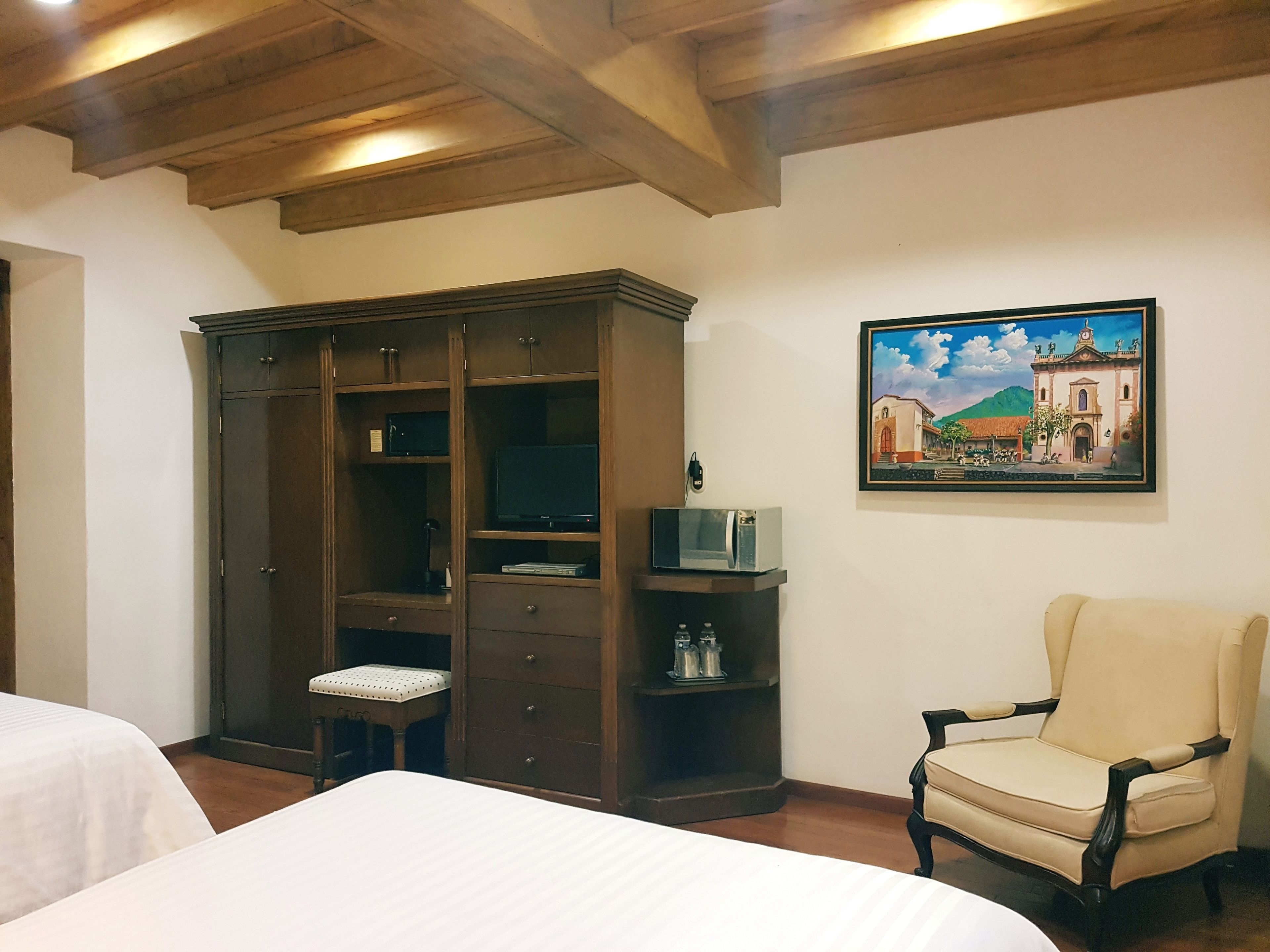 Un dormitorio con un armario grande, una silla, una cama y un cuadro en la pared.