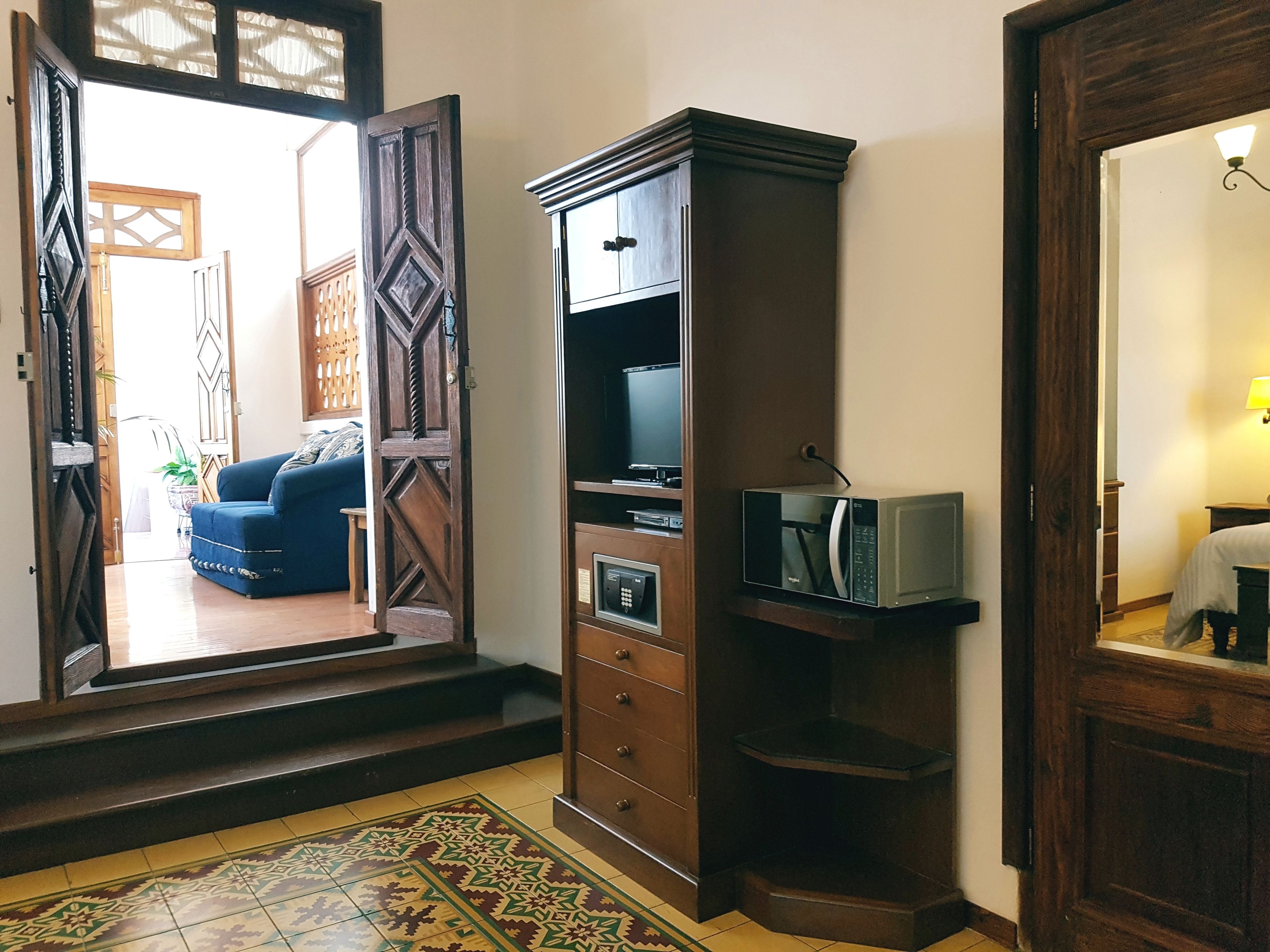 A hotel room with a wooden cabinet, a microwave, and a television. There is a patterned floor and a door leading to another room.