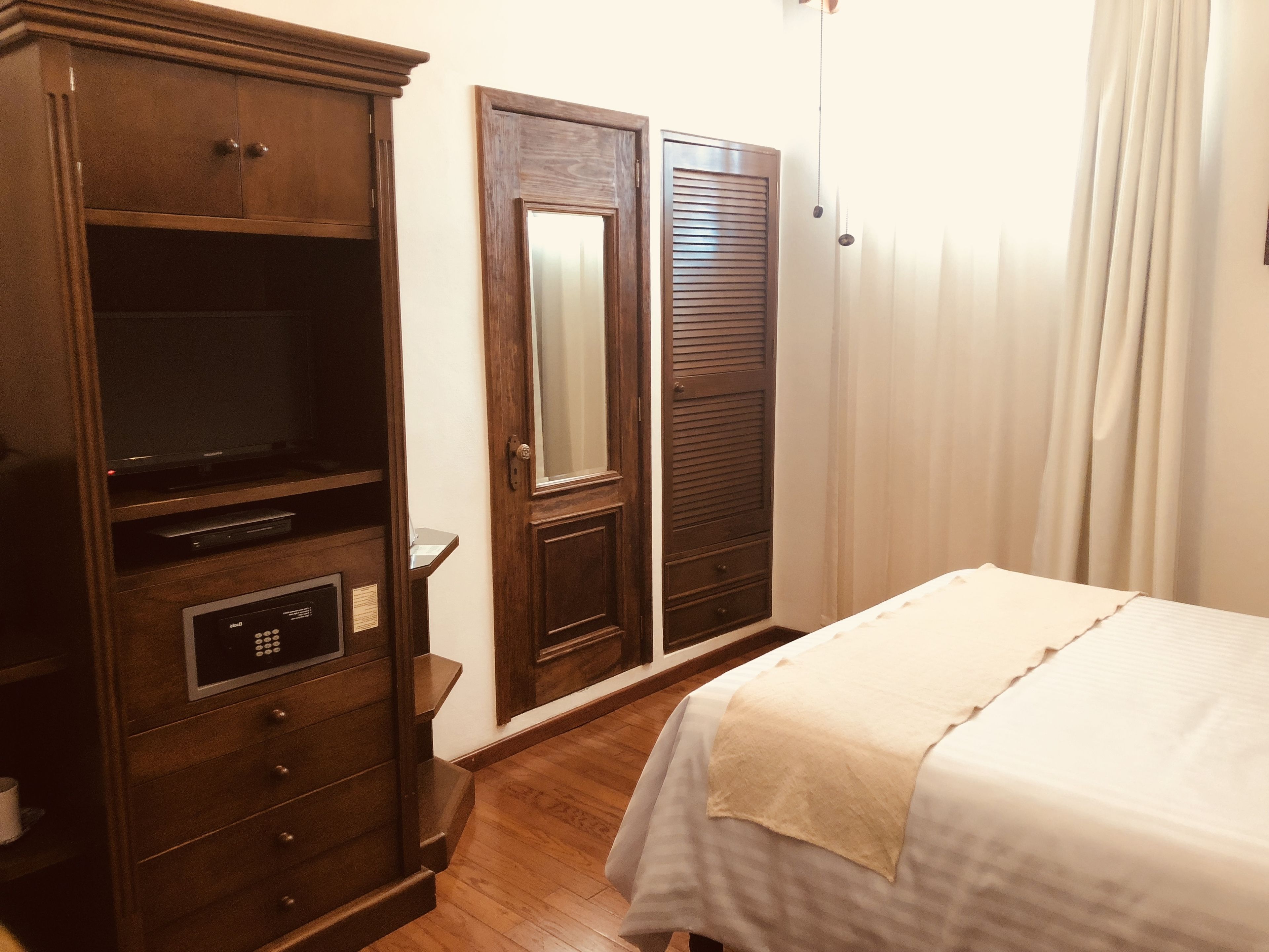 Una habitación de hotel con un armario de madera, una cama con colcha blanca y un espejo.