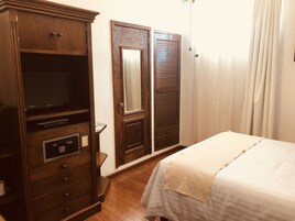 Una habitación de hotel con un armario de madera, una cama con colcha blanca y un espejo.