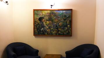 A room with wooden beams on the ceiling, two dark blue armchairs, a small wooden table, and a colorful painting on the wall.