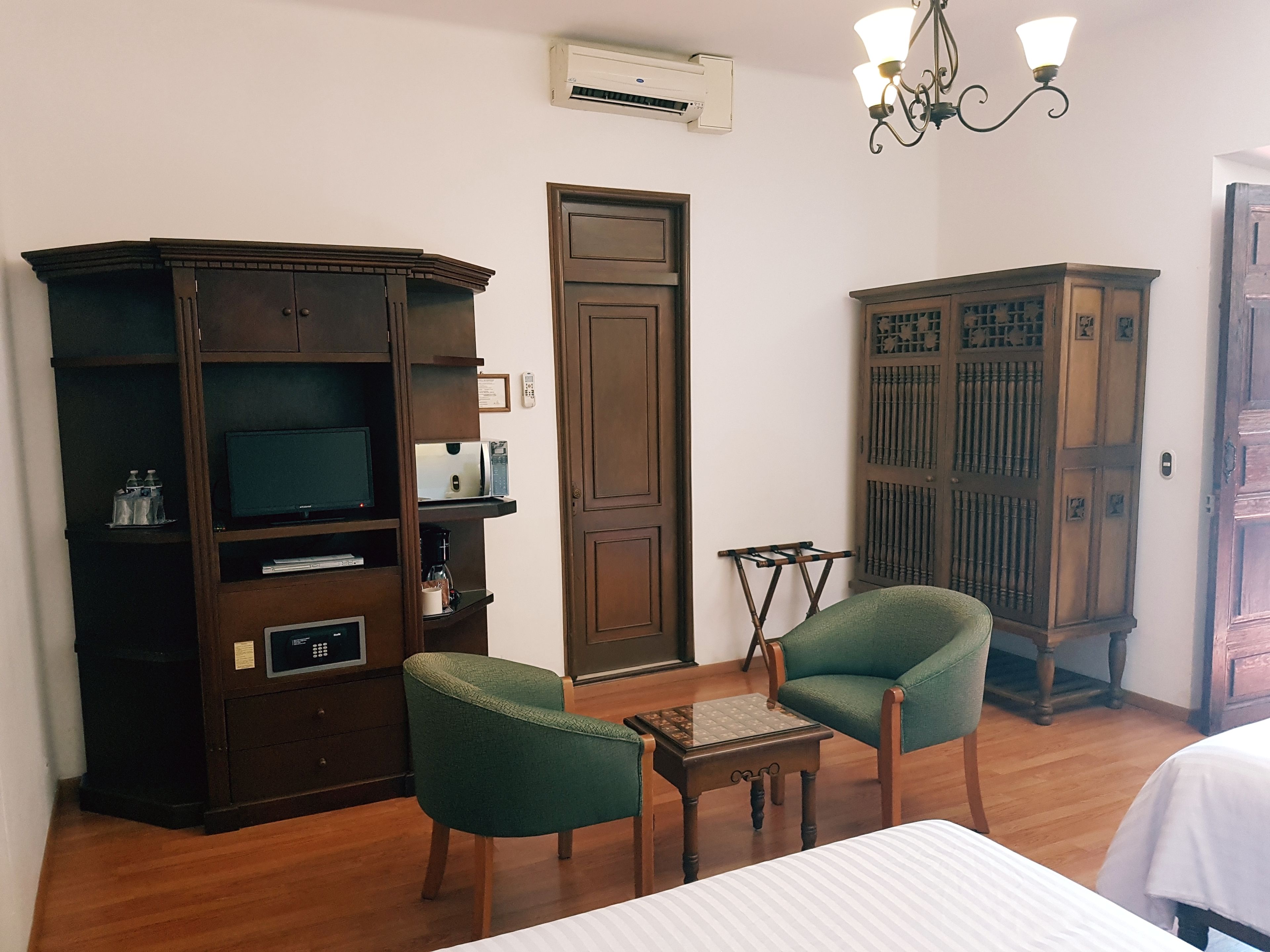 A room with a bed, two green armchairs, a small table, a TV, a coffee maker, and a cabinet.