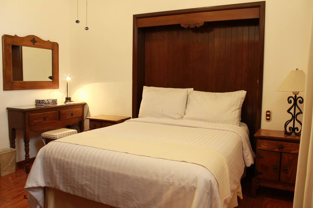 A neatly made bed with a wooden headboard, a bedside table with a lamp, and a dresser with drawers.