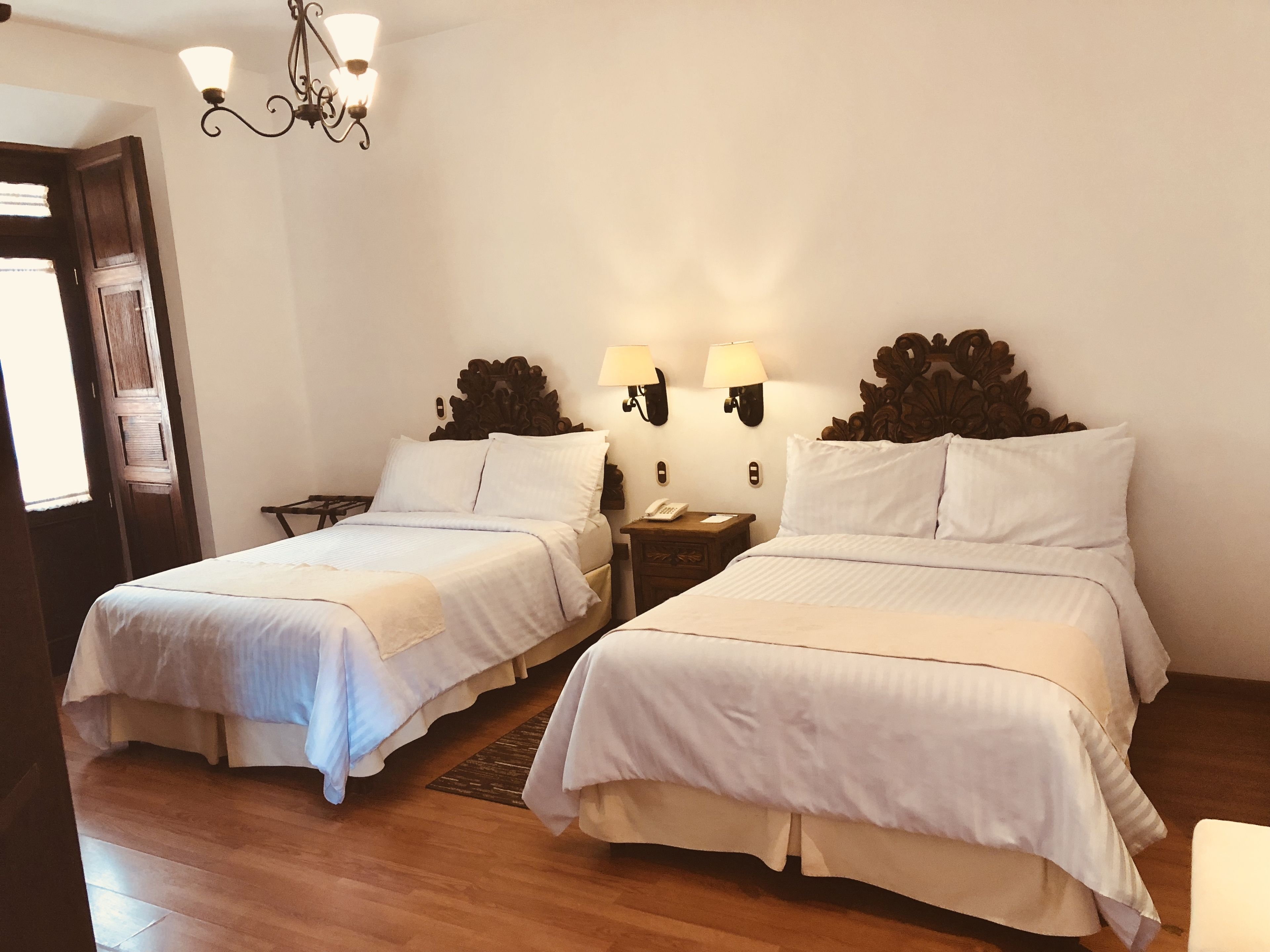 Habitación de hotel con dos camas individuales, suelo de madera, candelabro y lámparas de pared.