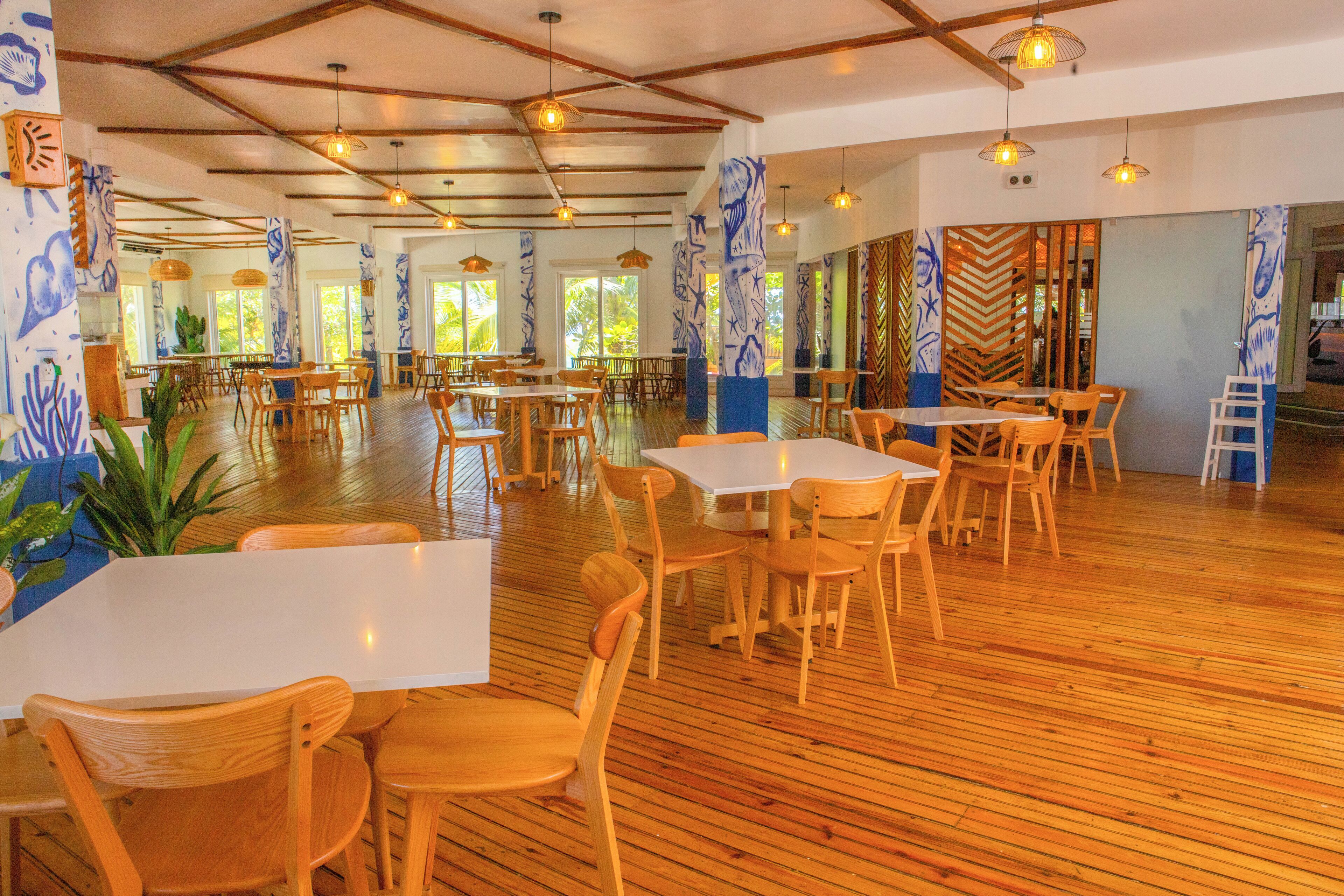 A spacious dining area with wooden tables and chairs, large windows, and decorative wall panels.