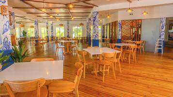 A spacious dining area with wooden tables and chairs, large windows, and decorative wall panels.