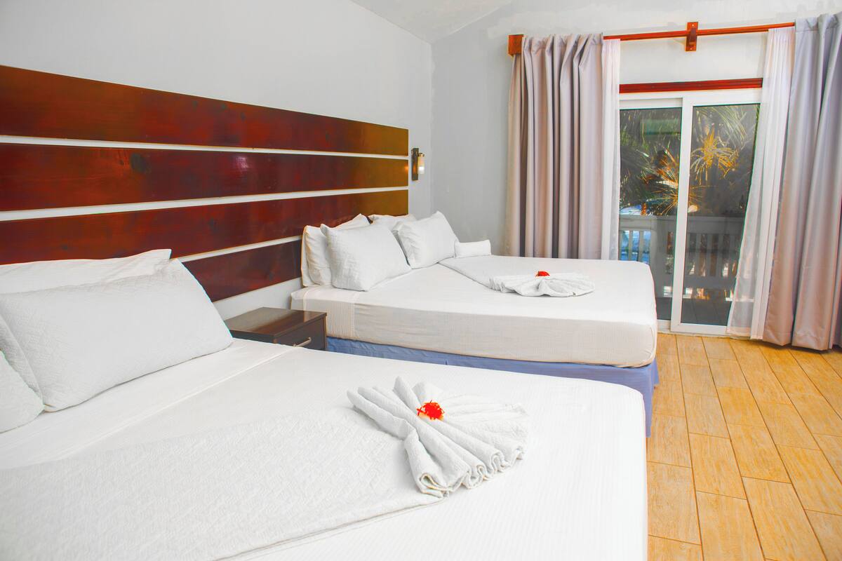 A hotel room with two beds, a wooden headboard, and a balcony with curtains.