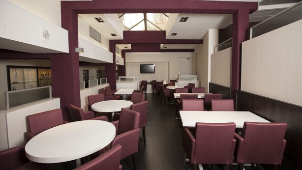 A modern restaurant with white tables and maroon chairs, featuring a high ceiling and natural light from windows. - Hotel Florida (Lourdes)